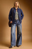 Woman wearing a blue shirt, striped top, and jeans against a brown background