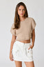 Woman wearing a beige ribbed top and white shorts on a plain background