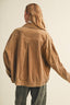 A person shown from the back wearing an oversized tan corduroy jacket and dark gray pants against a plain light beige studio background.