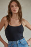 Woman wearing a black tank top and blue jeans against a neutral background
