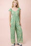 Woman wearing a green patterned jumpsuit on a pink background