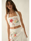 Woman wearing a white embroidered top and skirt with floral designs on a plain background