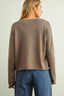 Person wearing a brown sweater and blue jeans on a plain background