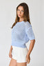 Woman wearing a light blue crochet top and white shorts on a plain background