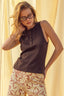 Woman wearing a brown sleeveless top and patterned pants against a beige curtain background