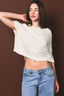 Woman wearing a white cropped sweater and blue jeans against a brown background
