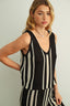 Woman wearing a black and white striped sleeveless top and pants against a plain background