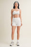 Woman wearing a white sports bra and shorts set on a plain background