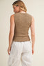 Woman wearing a textured beige sleeveless top and white pants on a plain background