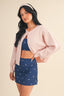 Woman wearing a pink cardigan, blue patterned top, and skirt on a beige background