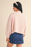 Woman wearing a light pink sweater and blue skirt with white patterns on a beige background