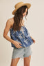 Woman wearing a blue patterned top and denim shorts with a straw hat on a plain background