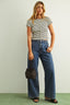Woman wearing a striped shirt and blue jeans holding a black handbag against a plain background