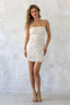 Woman wearing a white strapless lace dress against a plain background