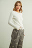 Woman wearing a white sweater and gray pants with bow patterns on a plain background