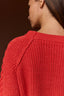 Close-up of a person wearing a chunky knit red sweater, shown from the back and side against a dark brown background.