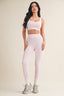 Woman wearing a light pink sports bra and leggings set on a beige background