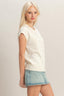 Woman wearing a white sleeveless top and denim skirt on a plain background