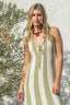 Woman wearing a green and white striped dress against a white wall with greenery.