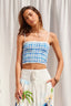 Woman wearing a blue and white checkered top with a white skirt against a white curtain background