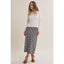 A woman modeling a white knit crewneck sweater and a navy and white plaid midi skirt, paired with black strappy high-heeled sandals, against a plain beige studio background.