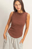 Woman wearing a brown sleeveless top and gray pants against a plain background