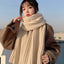 Person wearing a beige scarf and brown coat outdoors on a clear day
