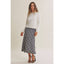 A woman modeling a white knit long-sleeve top and a navy and white plaid midi skirt, paired with black strappy high-heeled sandals, against a plain beige studio background.