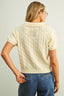Person wearing a cream-colored cable knit sweater and blue jeans against a plain background
