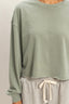 Sage green long-sleeve top worn with gray pants on a plain background