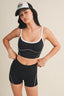 Woman wearing a black sports bra and shorts with a white cap on a beige background