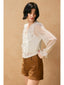 Woman wearing a white blouse with ruffles and brown shorts against a beige background