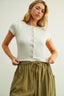 Woman wearing a white ribbed top and green striped pants on a plain background