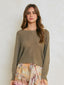 Woman wearing a green sweater and patterned skirt against a plain background