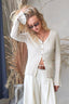 Woman wearing a cream-colored cardigan and white pants with a neutral background