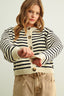 Young girl wearing a striped cardigan with beige pants on a plain background