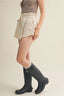 Person wearing a striped top, beige shorts, and dark rain boots on a plain background