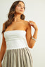 Woman wearing a white strapless top and beige pleated skirt on a plain background