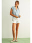 Woman wearing a light blue shirt and white shorts against a plain background