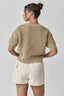 Woman wearing a beige knitted sweater and white shorts on a light gray background