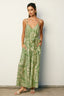 Woman wearing a green leaf-patterned dress against a white wall.
