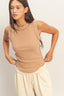Woman wearing a beige sleeveless top and light-colored pants against a plain background