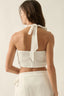 Woman wearing a white halter top with a bow detail on a beige background