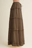 A brown tiered maxi skirt with ruffled trim and a side drawstring, shown on a mannequin against a plain beige background.