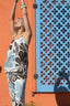 Person wearing a floral outfit against an orange wall with a decorative blue lattice.
