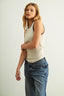 Woman wearing a beige tank top and blue jeans against a plain background