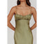 Woman wearing a green satin dress with thin straps on a plain background