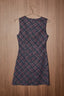 A sleeveless A-line dress with a blue and red plaid pattern, hanging on a metal hanger against a brown wood-paneled wall.