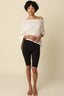 Woman wearing a white off-shoulder top and black leggings against a beige background