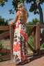 Woman wearing a floral dress with an open back, standing outdoors near a wooden fence.